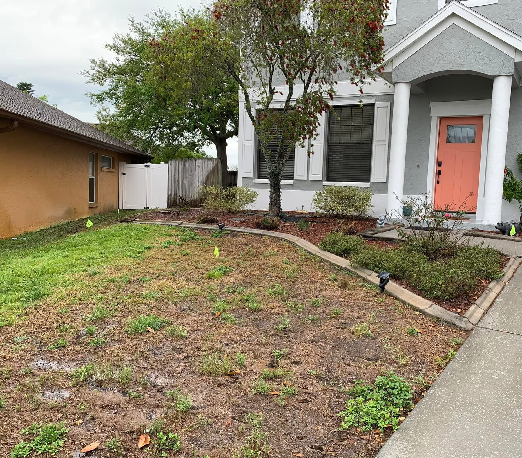 Front yard landscape before renovation with worn lawn, dated beds, and irrigation flags