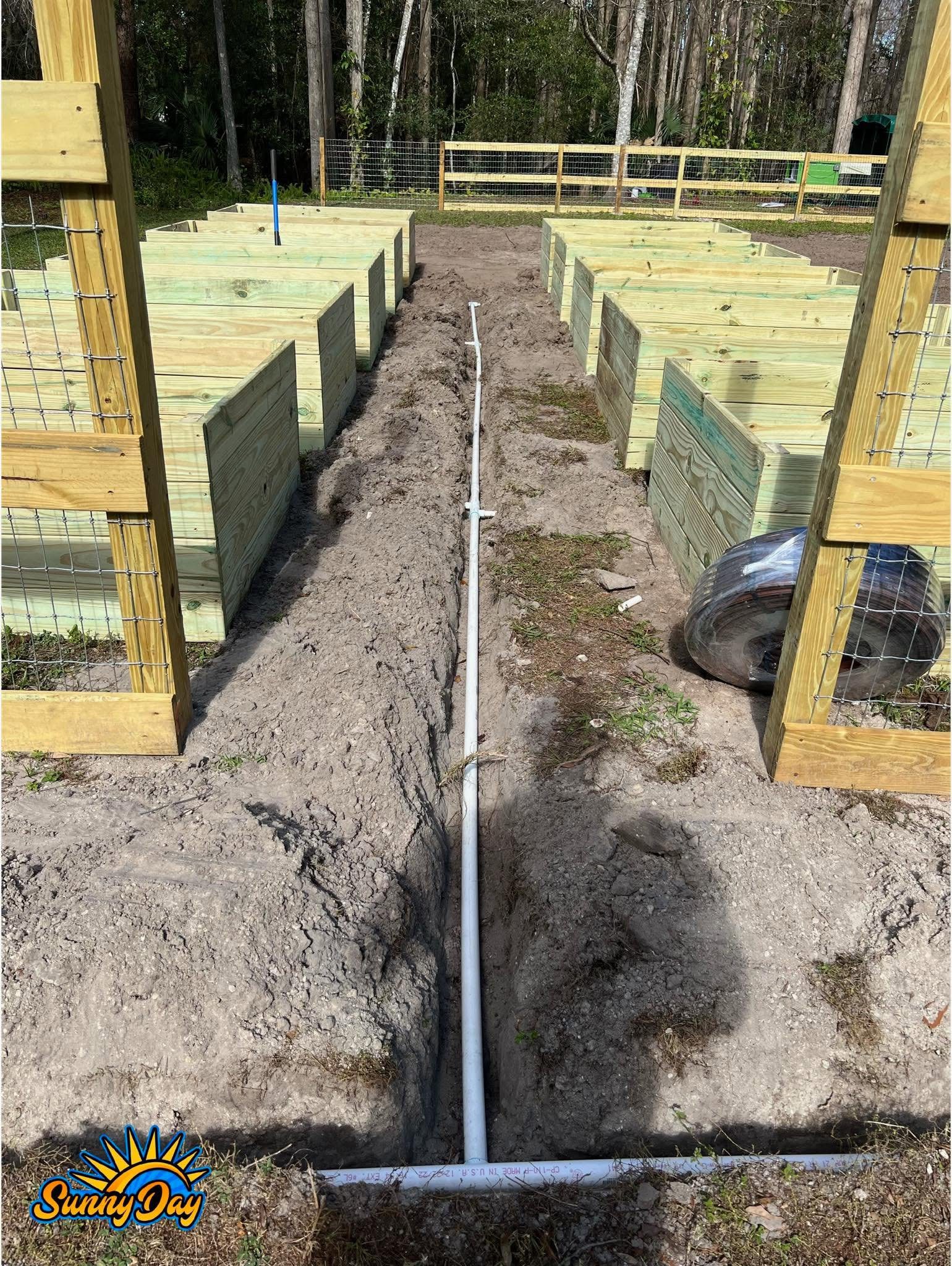 Irrigation line installation in progress with trench, PVC pipe, and raised garden beds