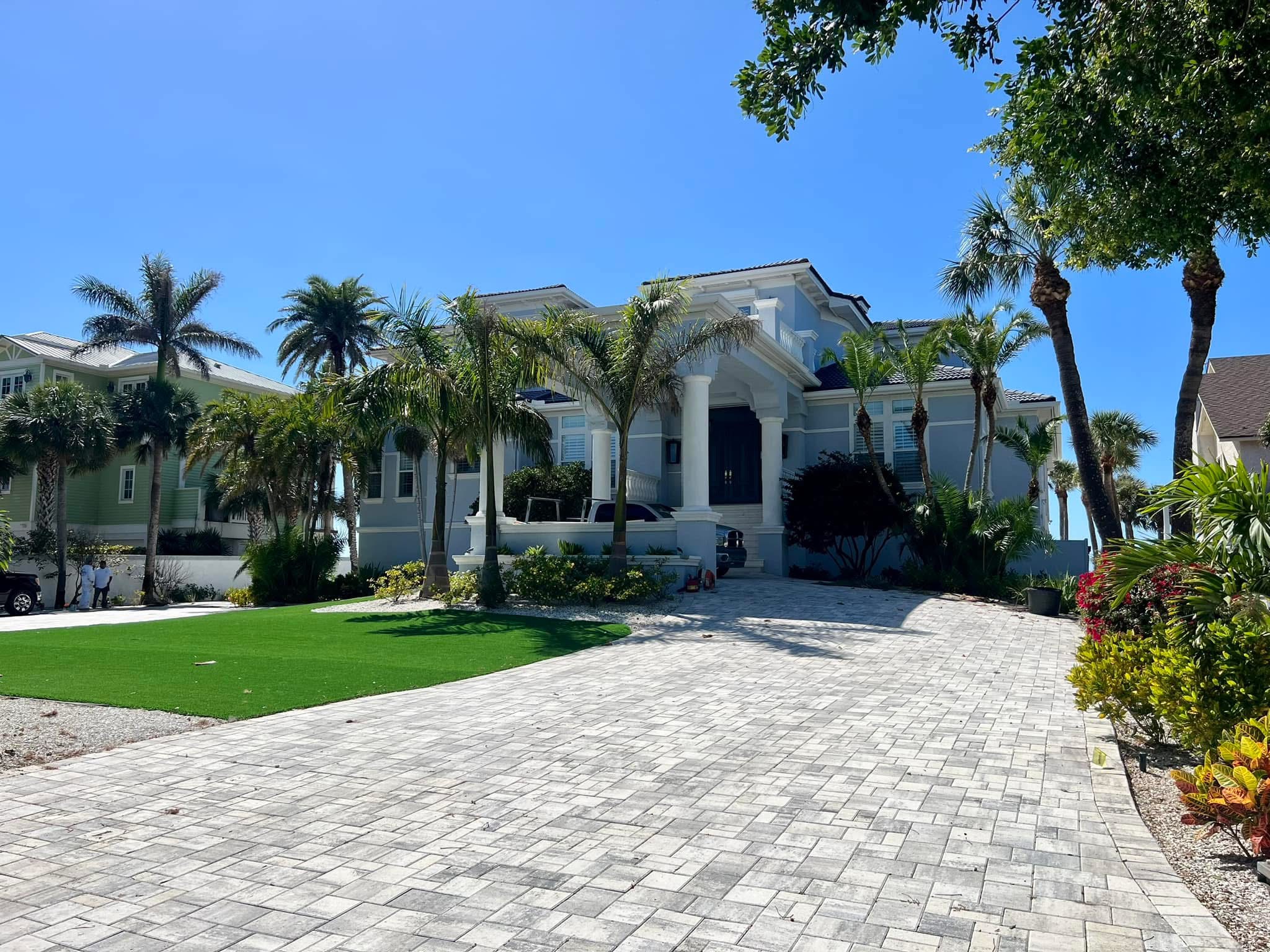 Luxury residential curb appeal with palm trees, paver driveway, and manicured landscape