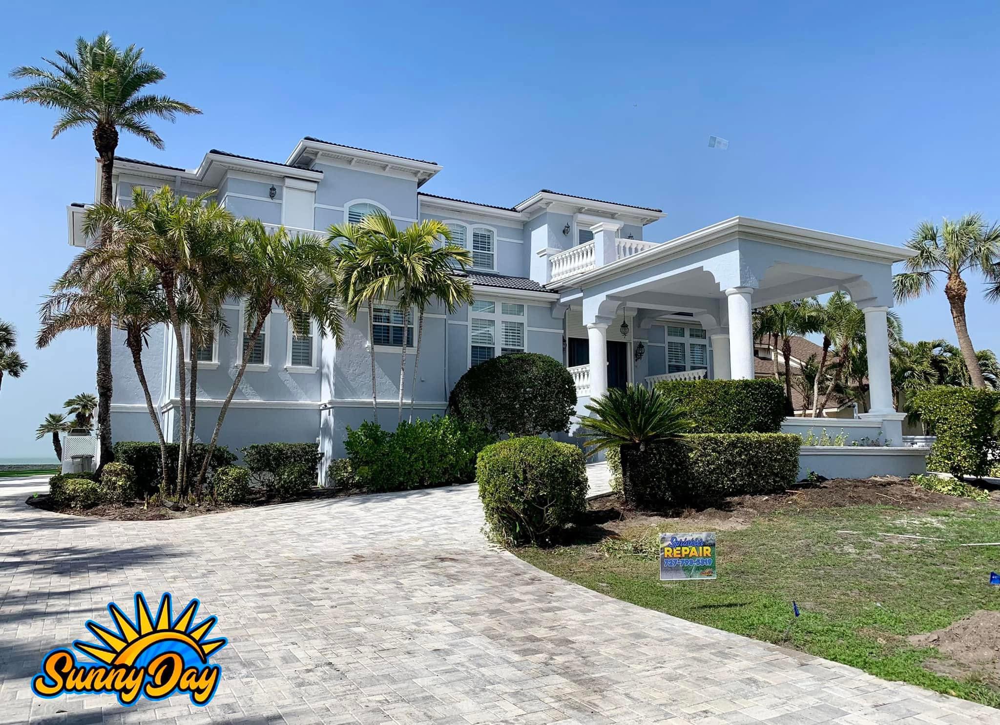 Luxury estate sprinkler repair with paver driveway, palms, and irrigation service marker