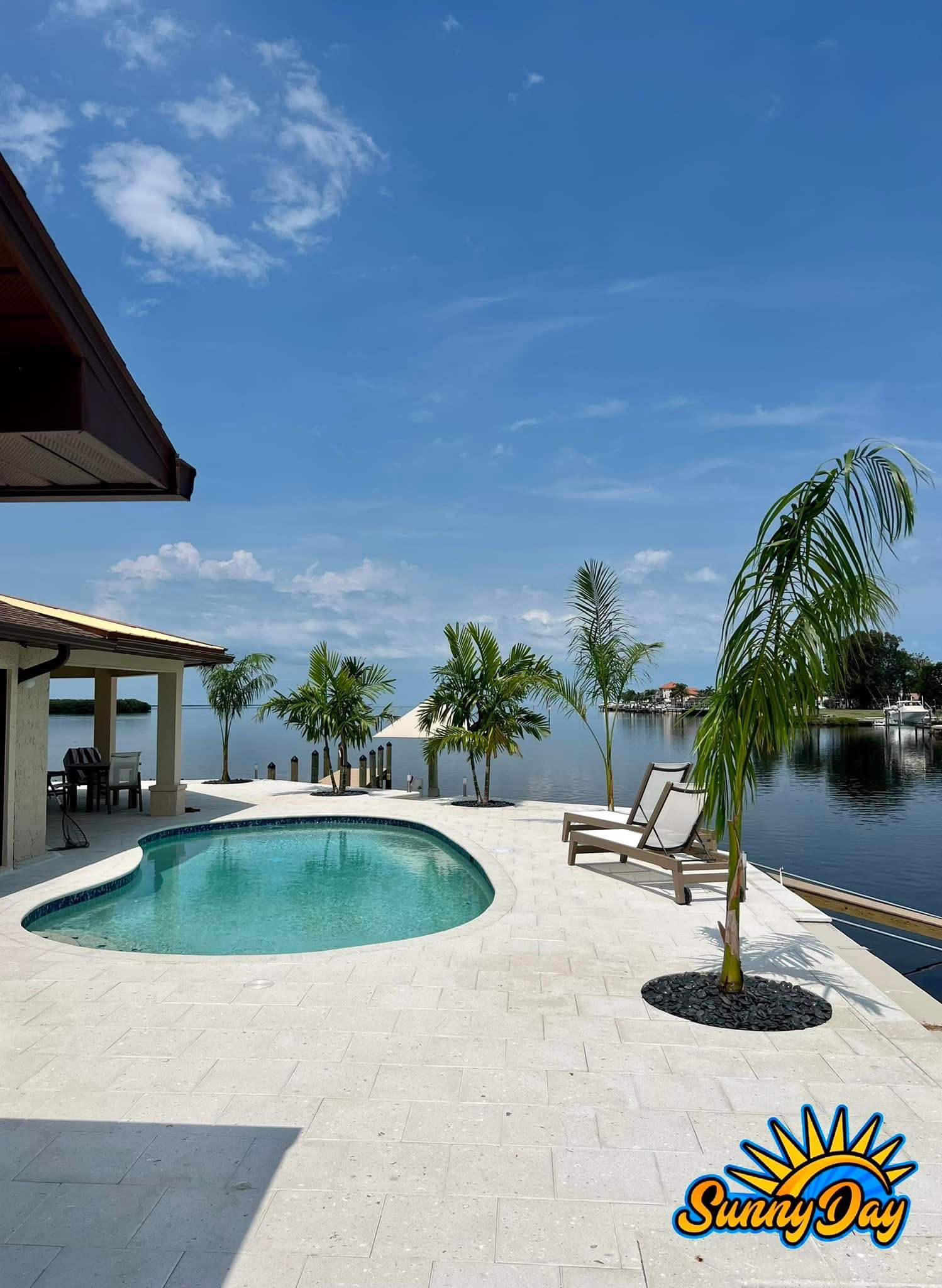 Waterfront pool patio with palms, white pavers, and modern outdoor finish