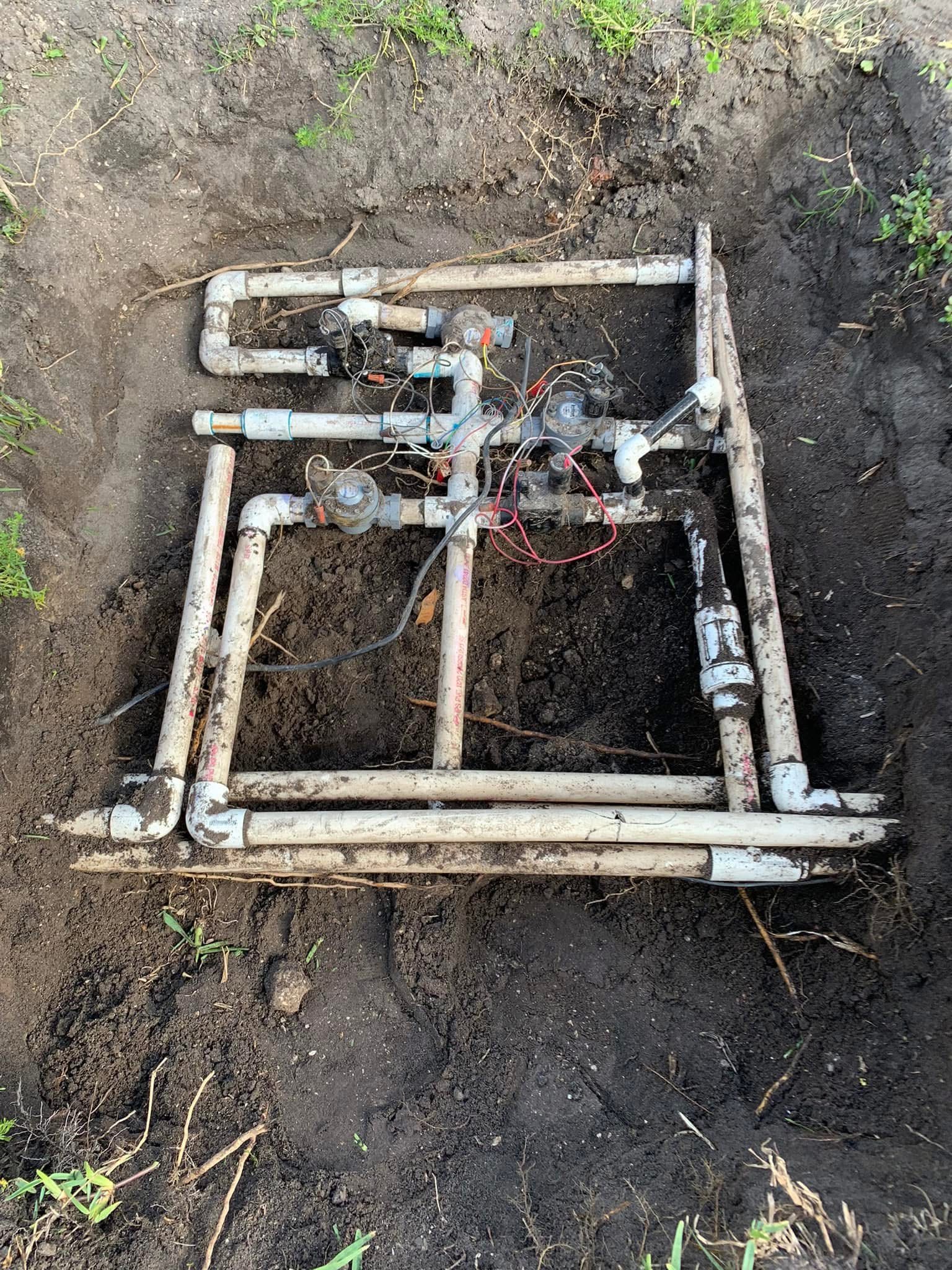 Old irrigation system before repair with exposed PVC pipes, valves, wiring, and trench work